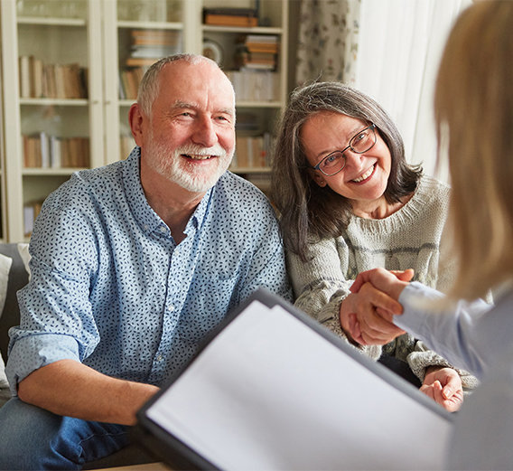 Mortgage renewal: Elderly couple shaking hands with mortgage broker in their home.